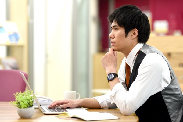 Young male office worker thinking while working on laptop in office